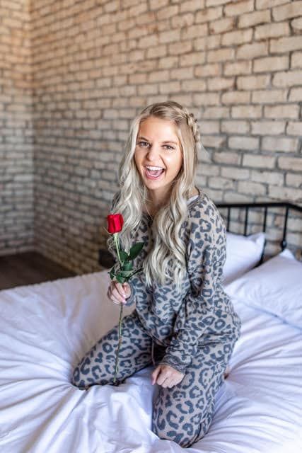 A woman is kneeling on a bed holding a rose.