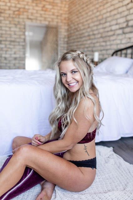 A woman in lingerie is sitting on the floor in front of a bed.