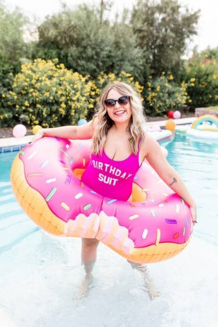 A woman in a pink swimsuit is holding an inflatable donut in a pool.