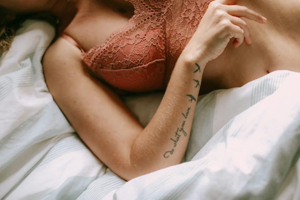 A woman is laying in bed with a tattoo on her arm.