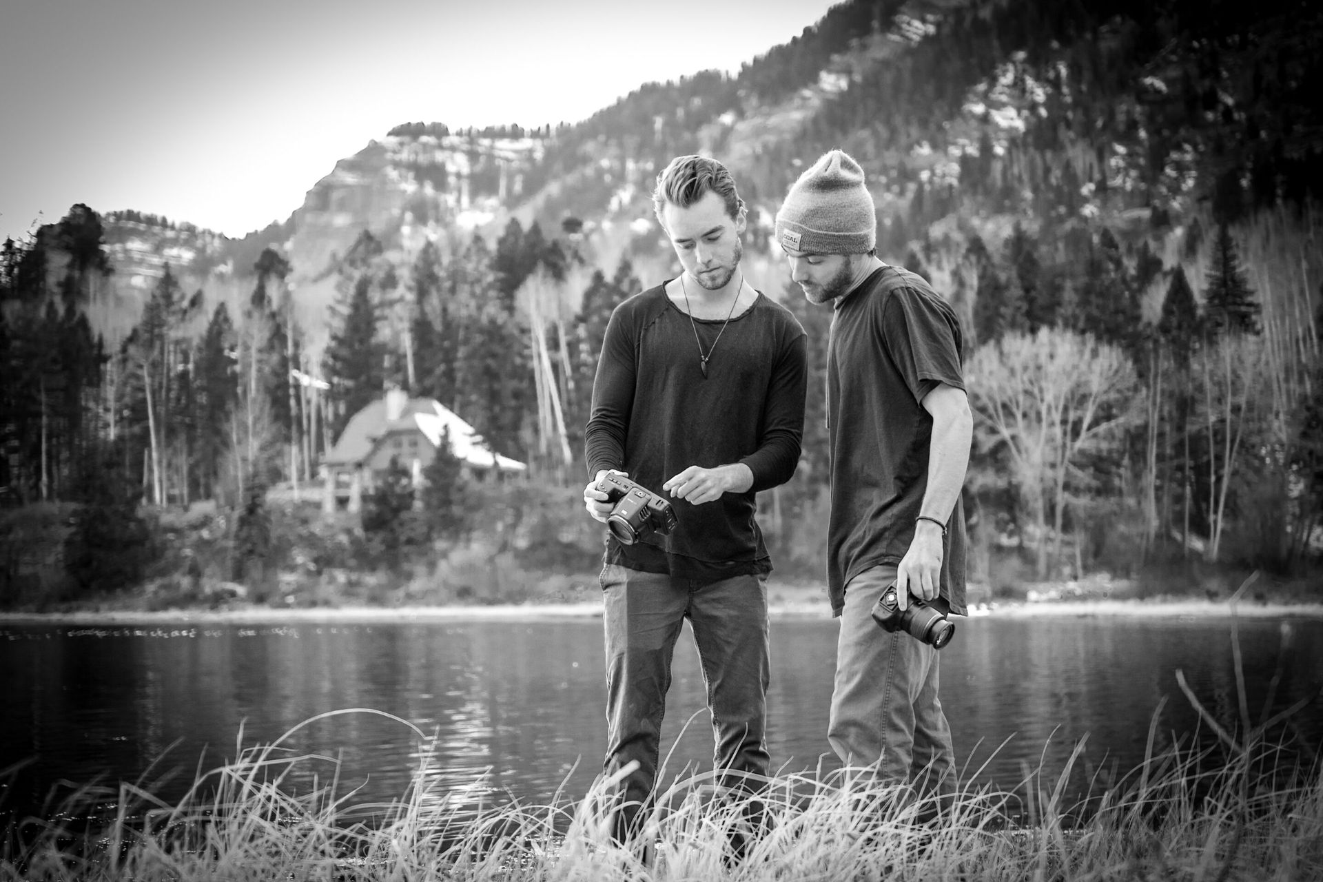 Two men are standing next to a lake looking at a camera.