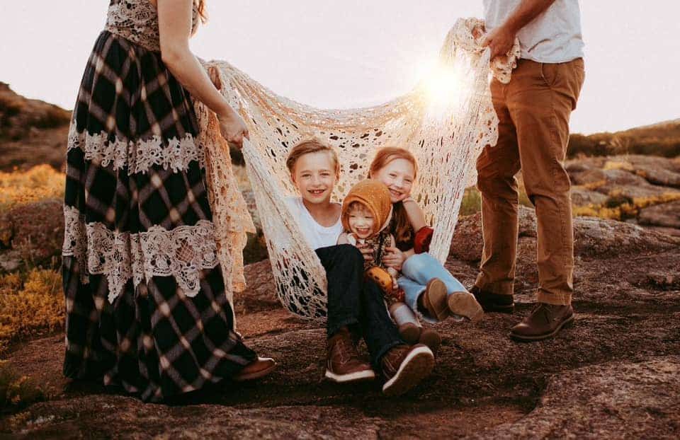 A family is sitting in a hammock on top of a rock.