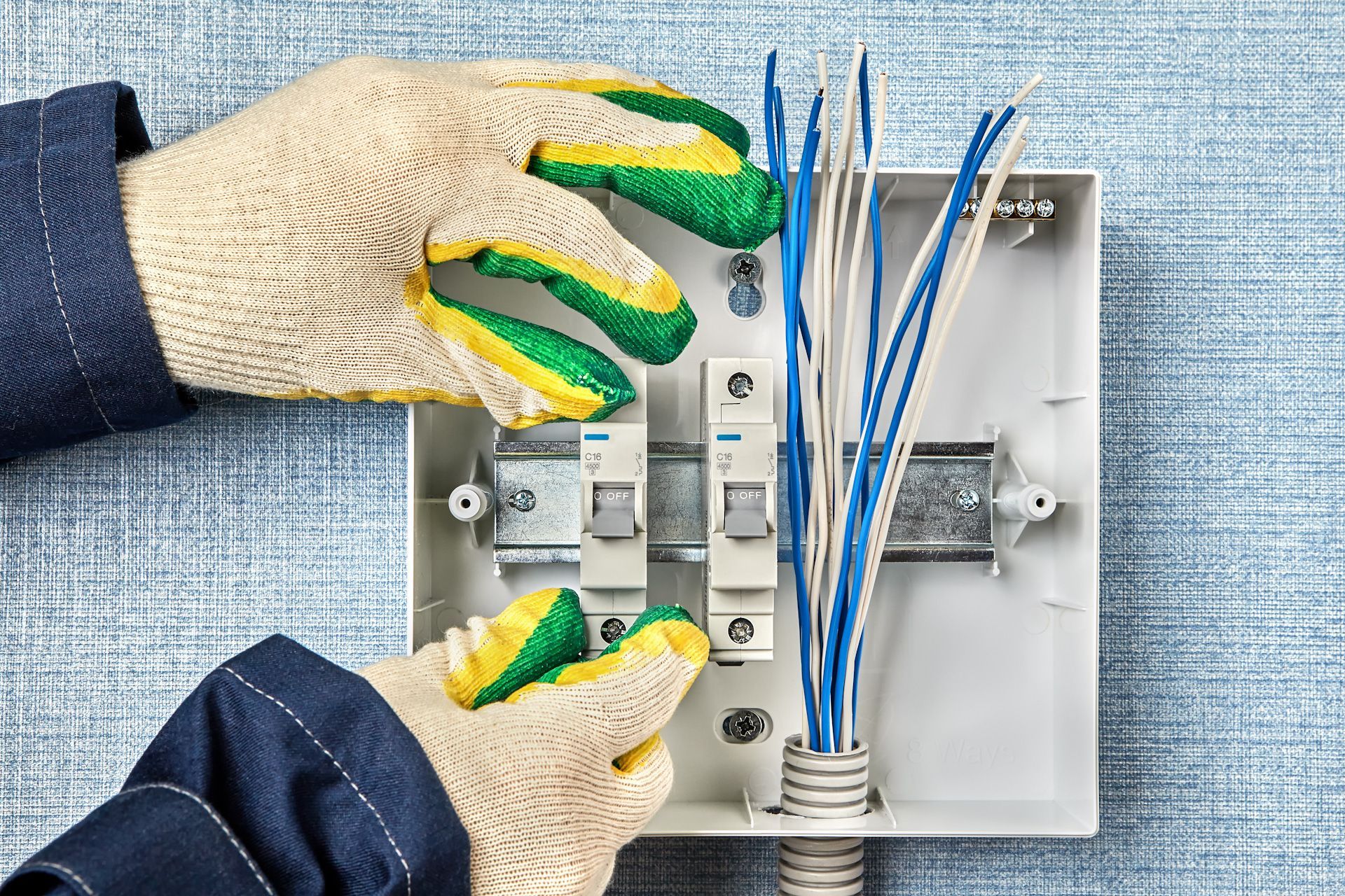 A person wearing gloves is working on an electrical box.