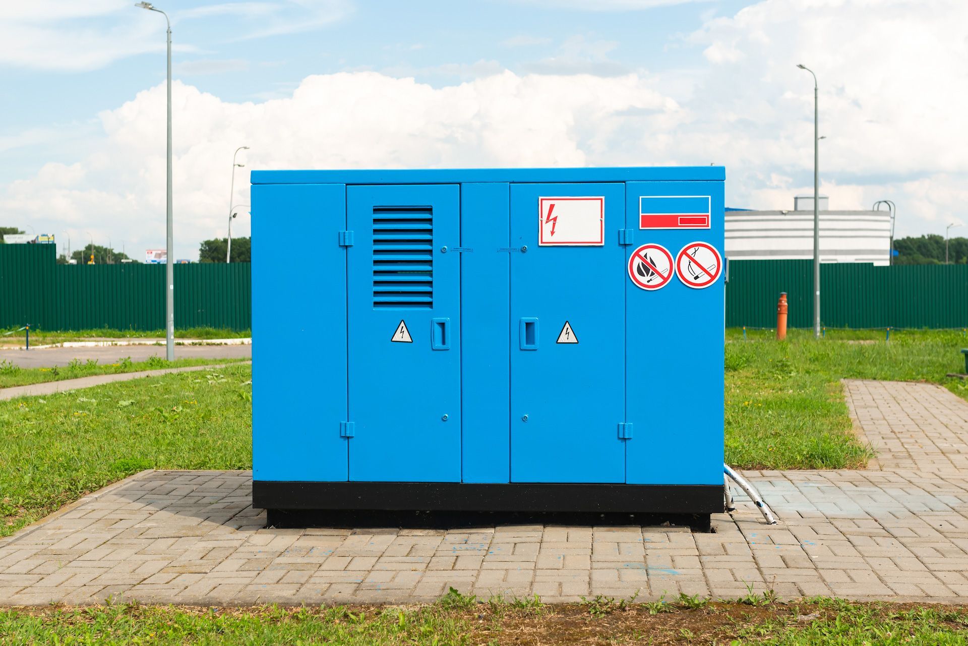 A blue box is sitting on a brick sidewalk in a grassy field.