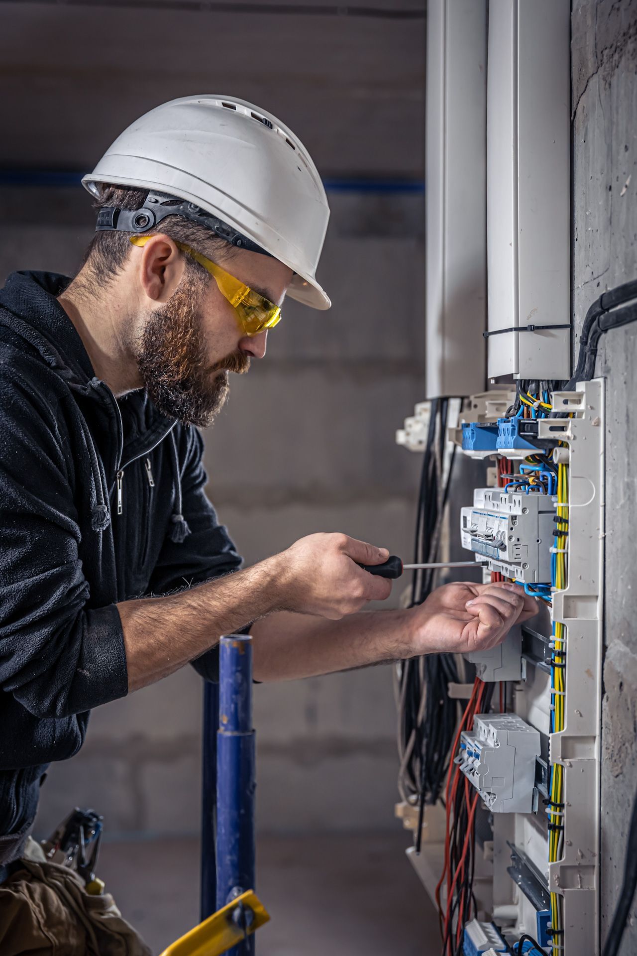 A man wearing a hard hat and safety glasses is working on an electrical box.