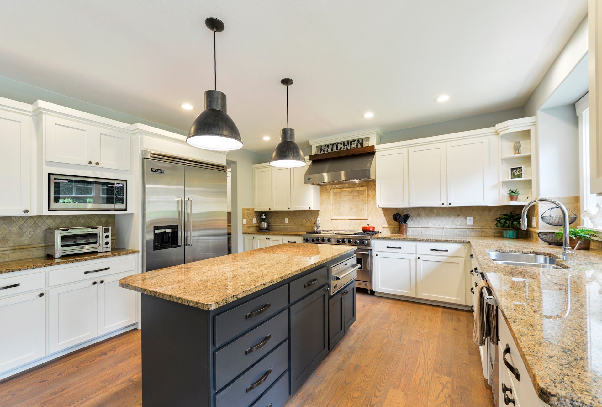 A kitchen with white cabinets , granite counter tops , stainless steel appliances and a large island.