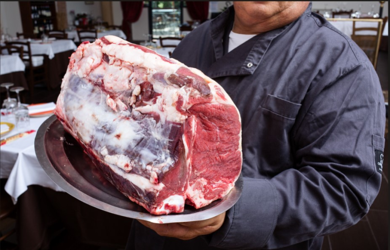 Uno chef tiene in mano un grande arrosto di manzo crudo su un piatto d'argento in un ristorante.