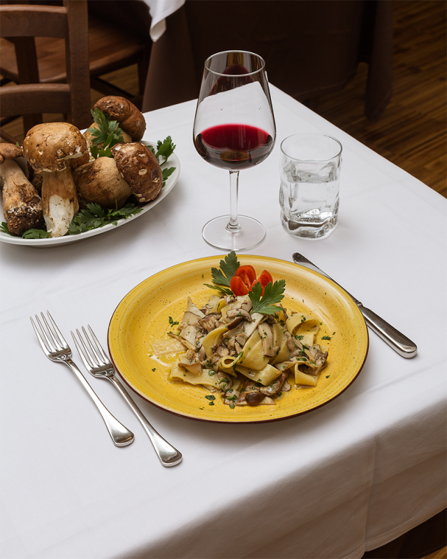 Pasta ai funghi, vino rosso, bicchiere d'acqua e funghi crudi su una tavola apparecchiata per cena.
