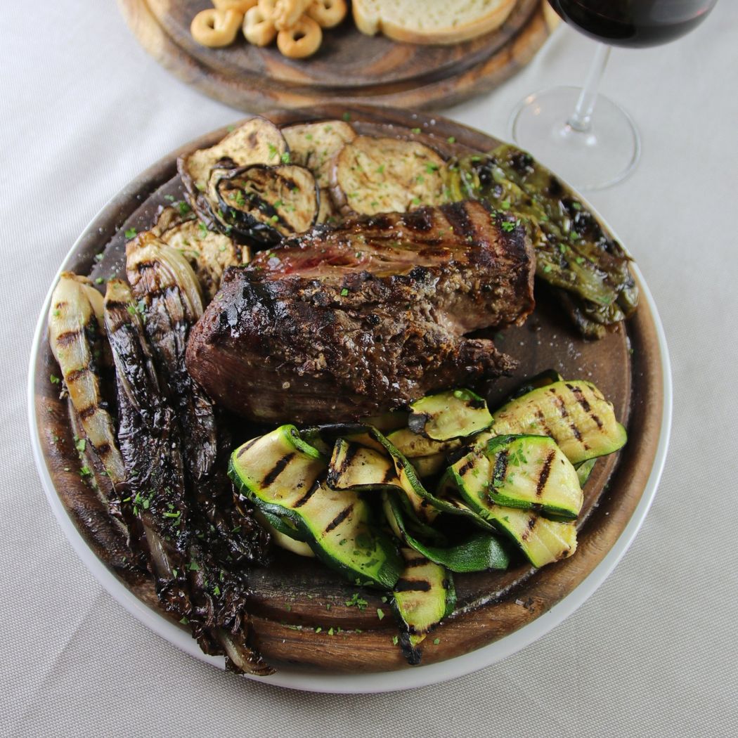 Bistecca alla griglia con verdure grigliate miste su un vassoio di legno, vino rosso in un bicchiere.