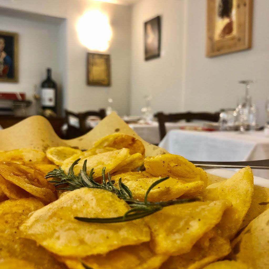 Primo piano di patatine dorate con rametto di rosmarino, disposte su un tavolo in un ristorante.