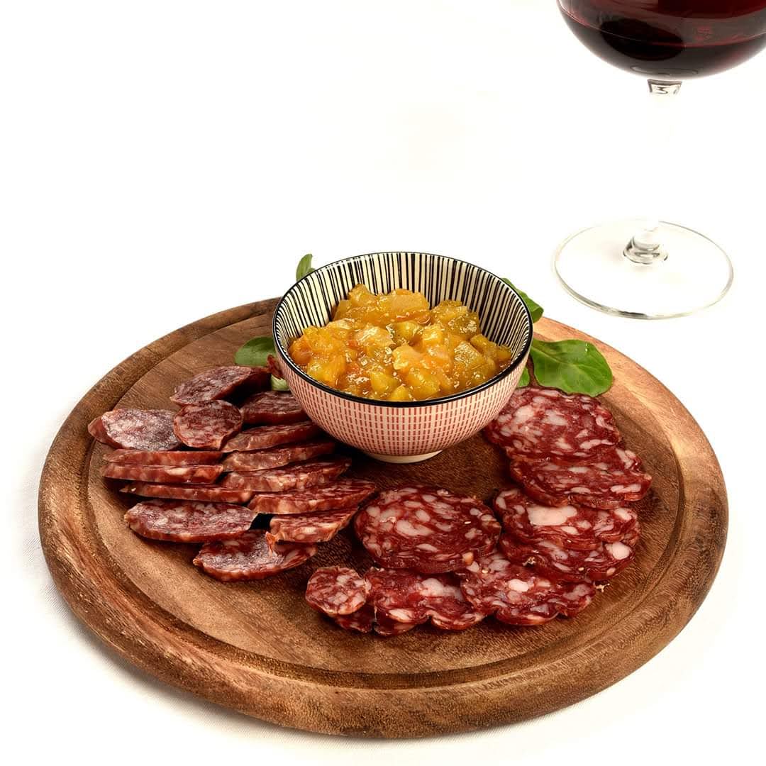 Piatto di legno con salame affettato, chutney di arancia e un bicchiere di vino.