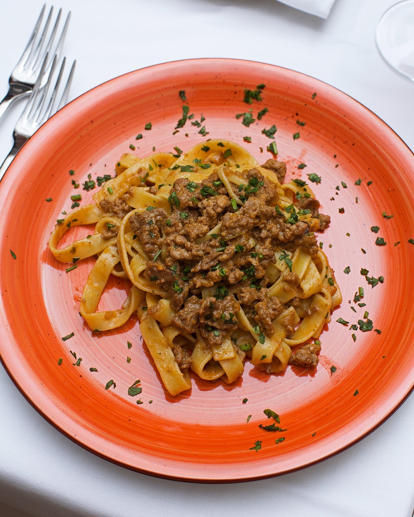 Piatto di pasta al ragù su un piatto arancione, guarnito con prezzemolo.
