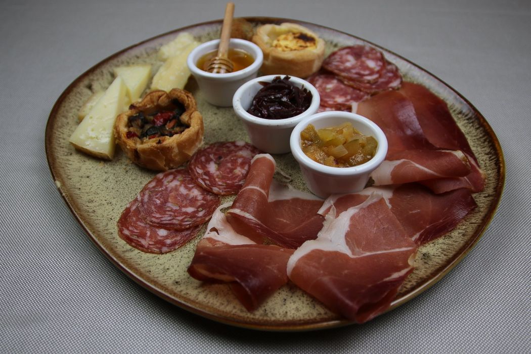 Piatto di salumi con salumi, formaggi e piccole salse su un piatto punteggiato.