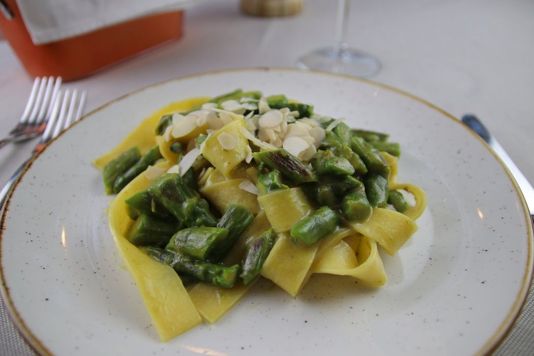 Pasta con fagiolini e mandorle a lamelle su un piatto bianco, ambientazione ristorante.