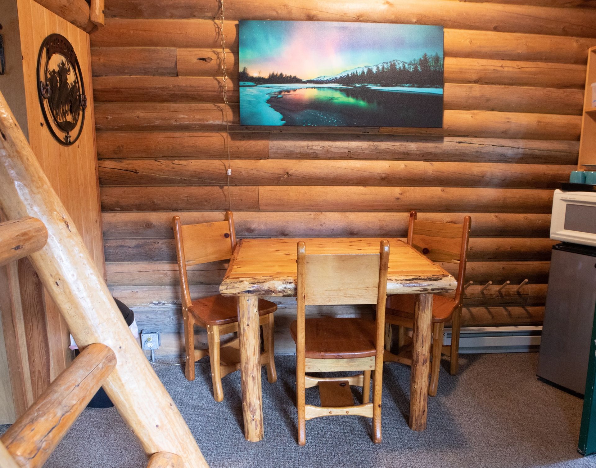 A wooden table and chairs in a log cabin with a painting on the wall.