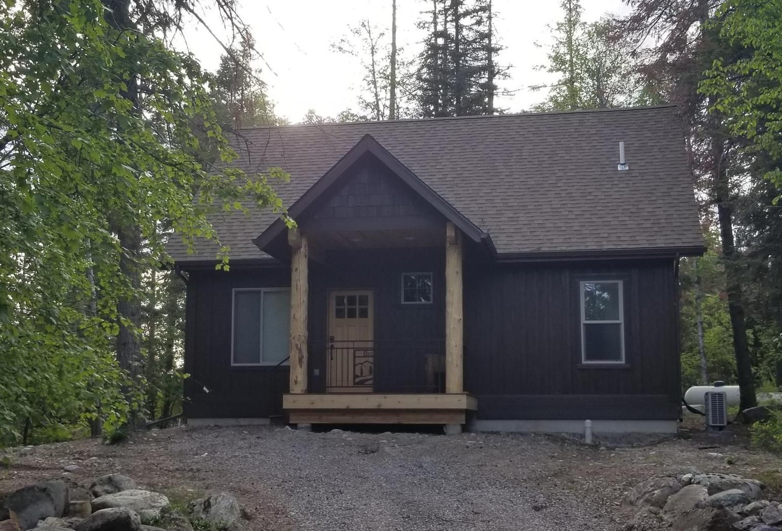 A small black house with a porch surrounded by trees