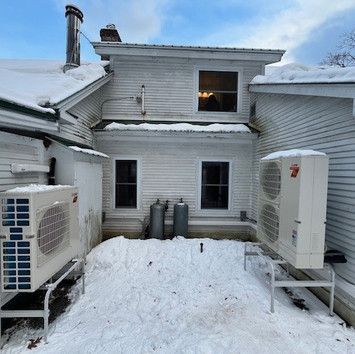 Two air conditioners are sitting in the snow in front of a house.