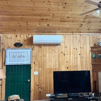 A living room with wood paneling , a flat screen tv , and a ceiling fan.