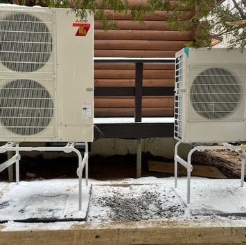 Two air conditioners are sitting next to each other in the snow.