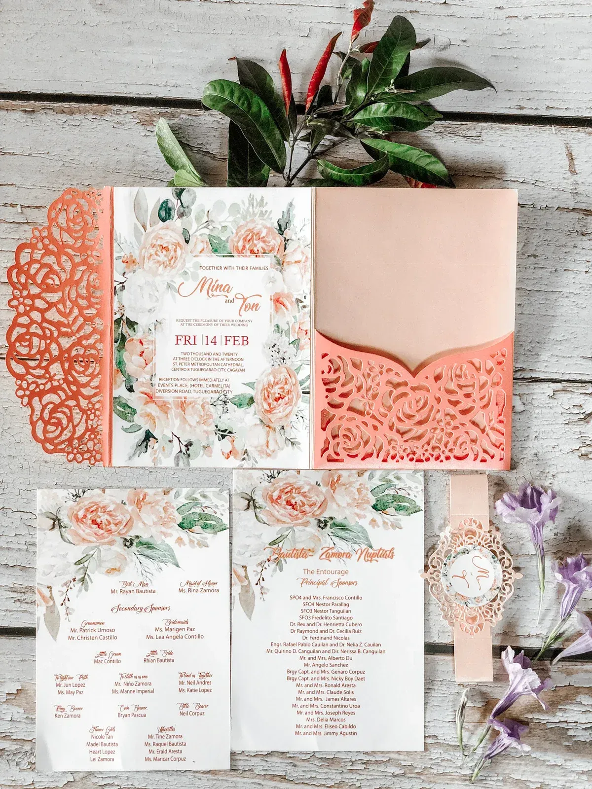 Peach floral wedding invitations and accessories on a wooden background.