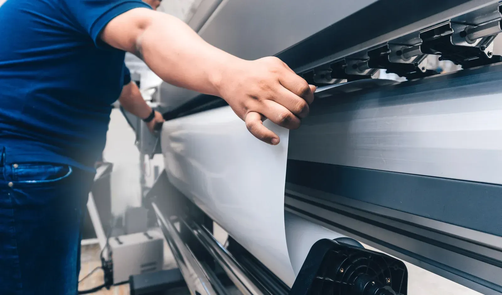 Person operating a large format printer, loading white material.