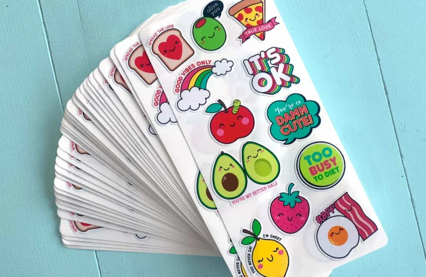 Stack of sticker sheets with food-themed and encouraging designs, including pizza, avocado, and 