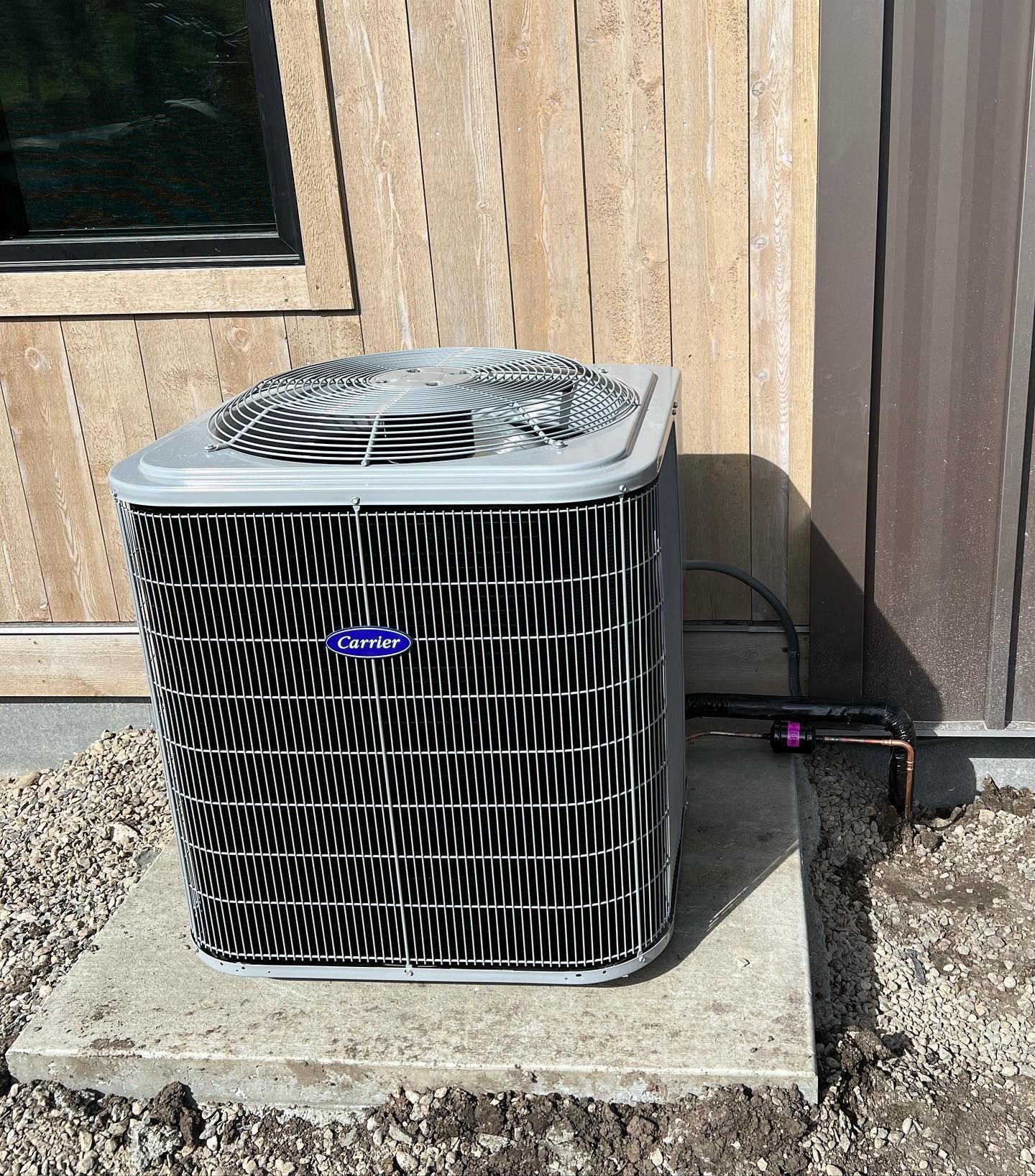 Outdoor air conditioner unit beside a tan wooden wall on a gravel pad