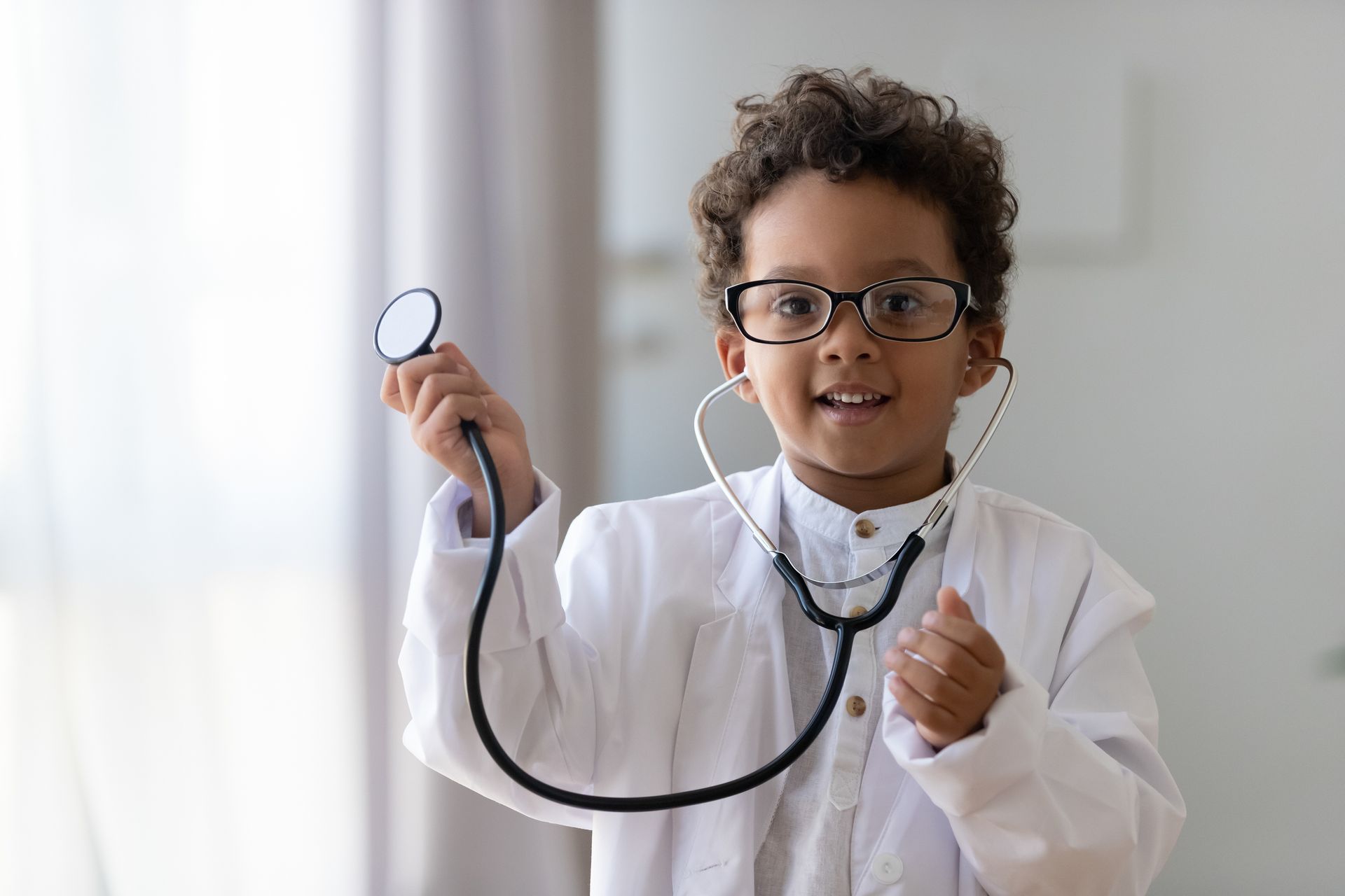 Little boy in a doctor's coat holding a stethoscope up