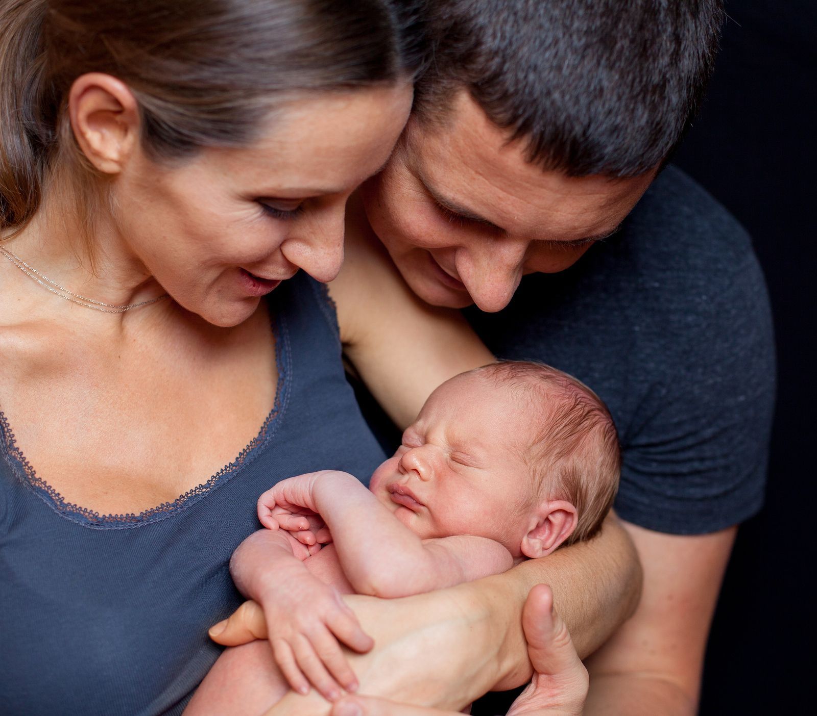 Parents holding a newborn infant and smiling down at the baby