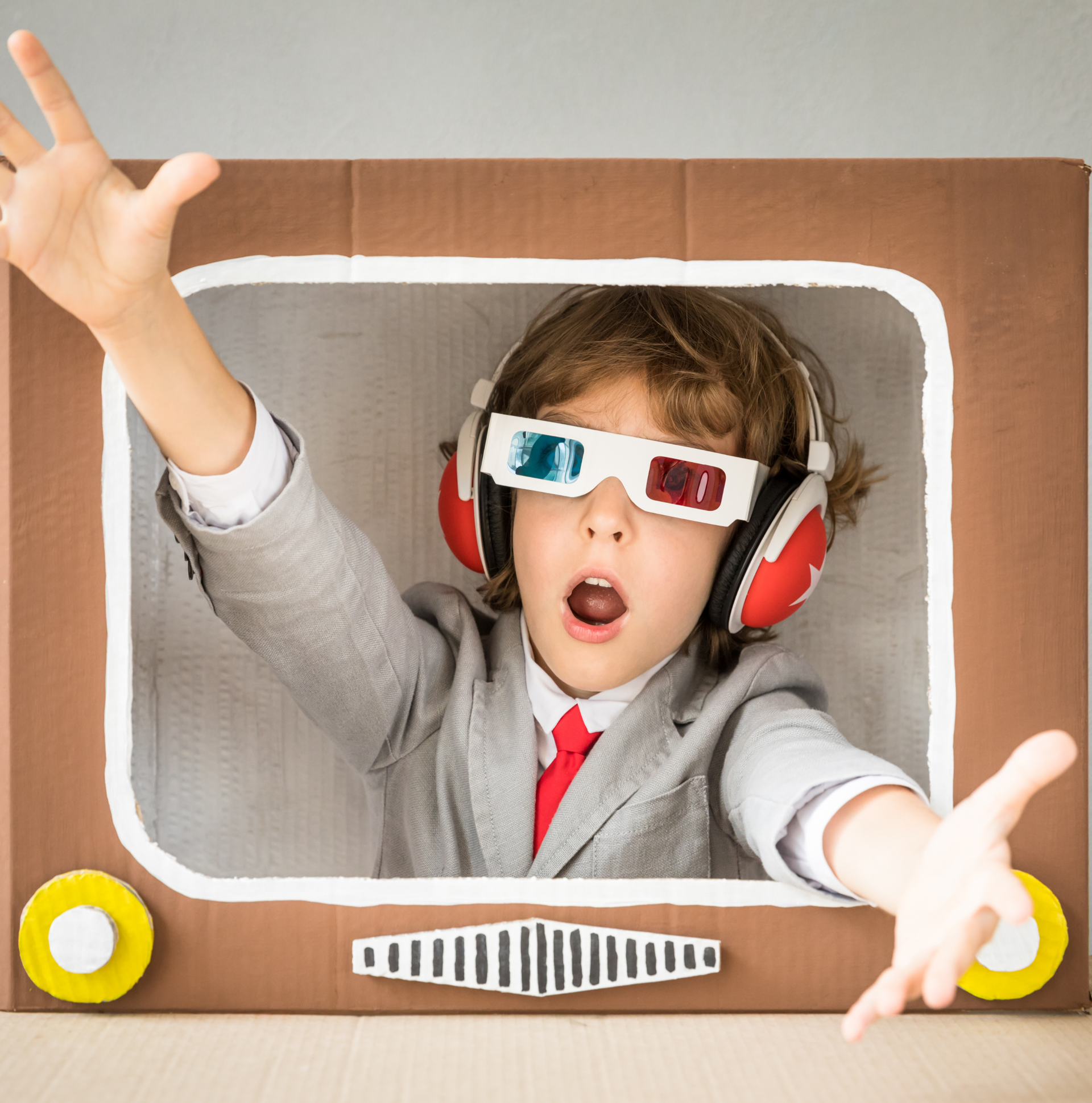 A young boy wearing 3d glasses and headphones is in a cardboard box