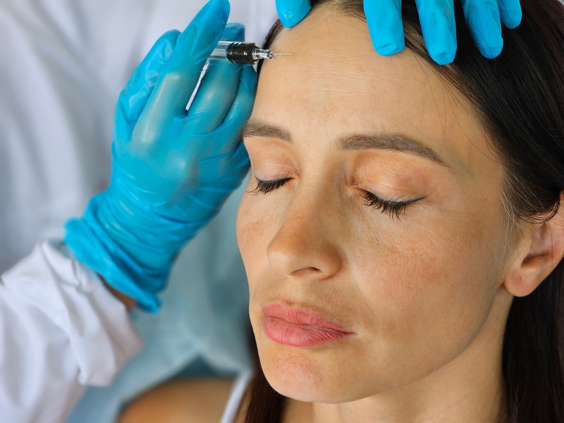 A woman is getting a botox injection in her forehead.