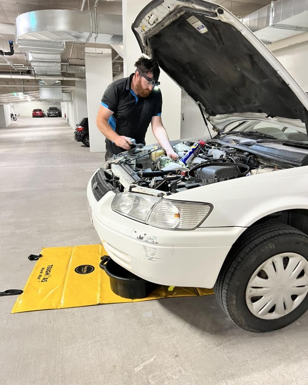 A Man Is Working On The Engine Of A Car In A Parking Garage — Weyba Automotive Services In Kuluin, QLD