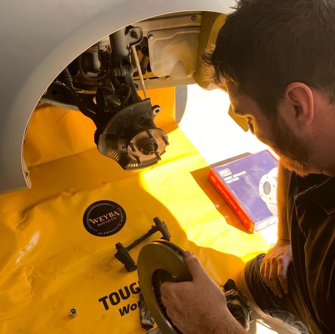 A Man Is Working On A Car On A Yellow Tough Work Mat — Weyba Automotive Services In Kuluin, QLD