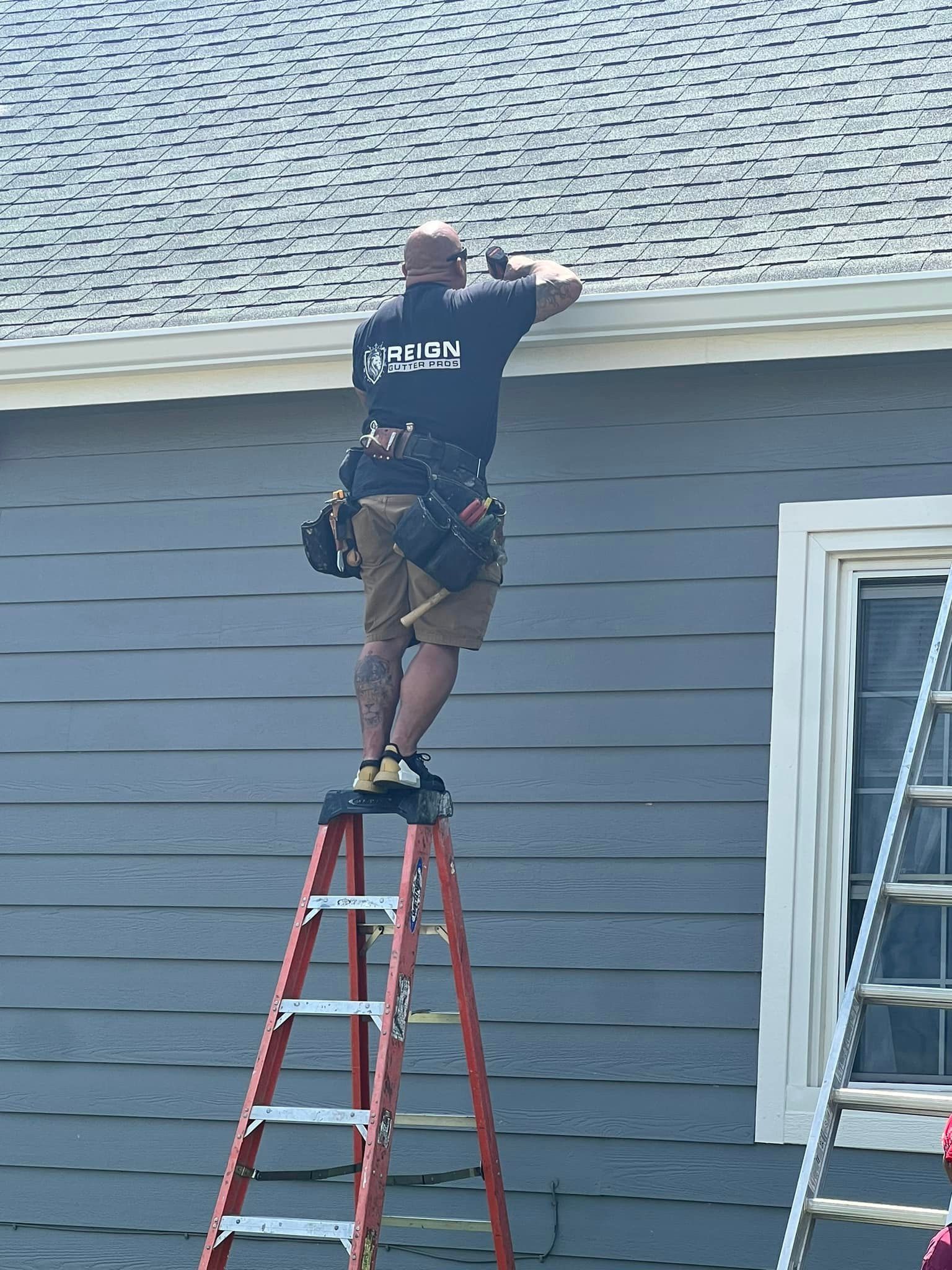 A man is standing on a ladder working on the roof of a house.