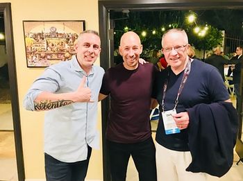 Three men are posing for a picture and one has a tattoo on his arm that says relentless