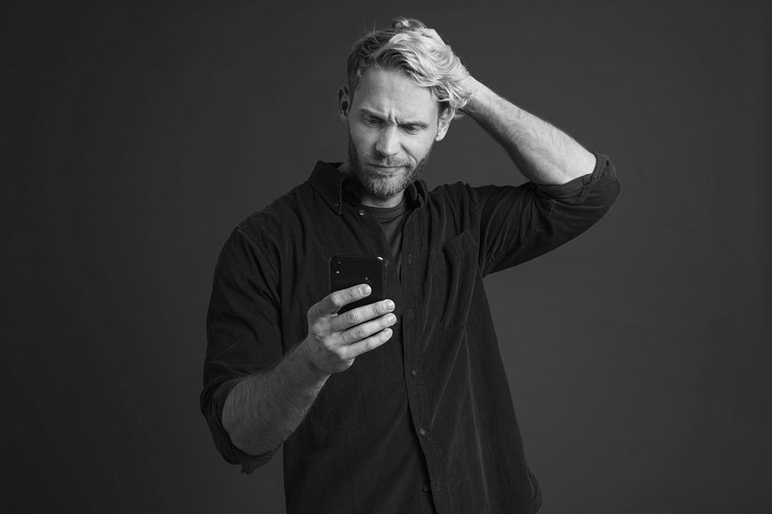 A man is holding his head while looking at his cell phone.