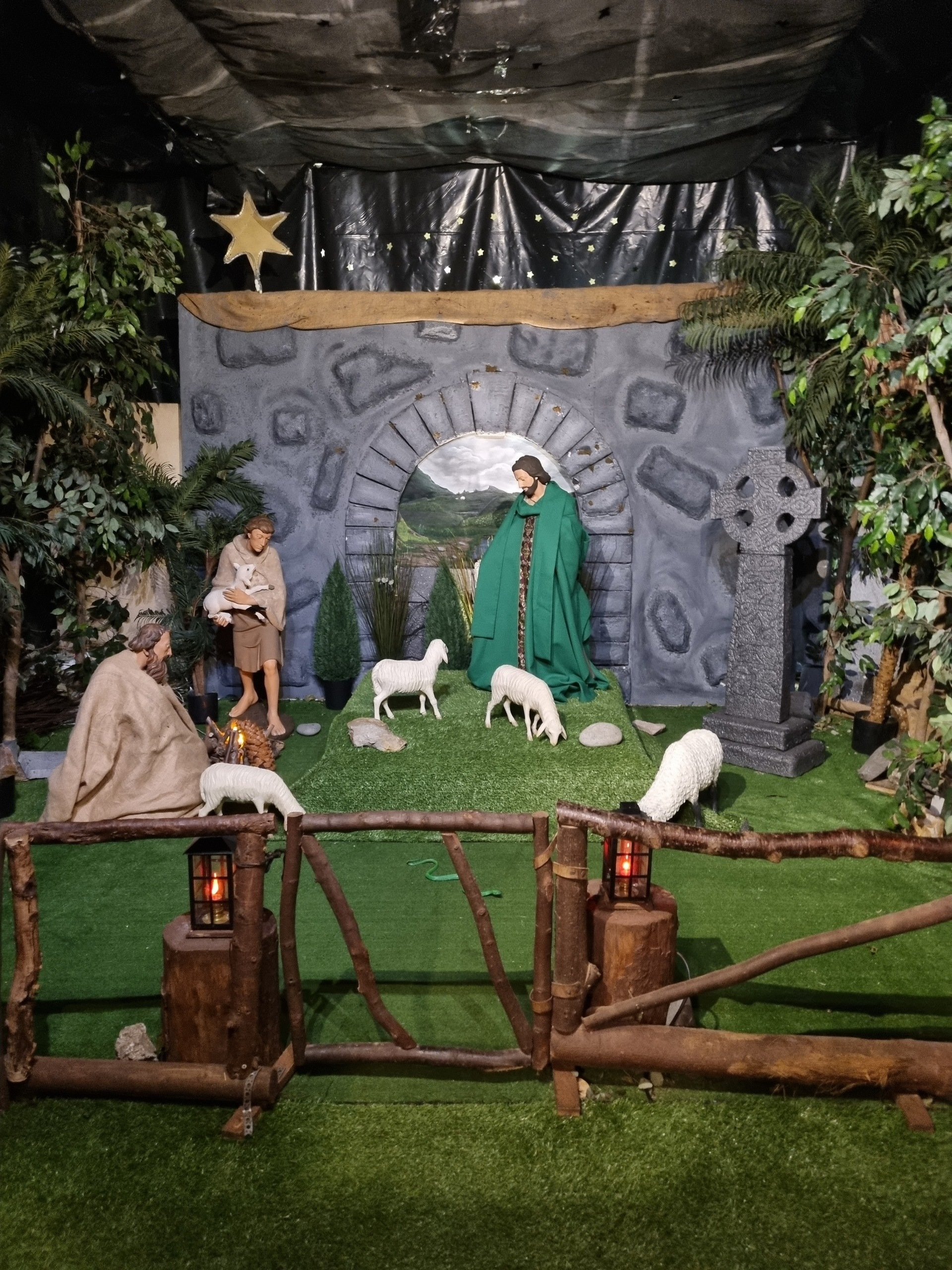 A nativity scene with a fence and sheep in the grass.
