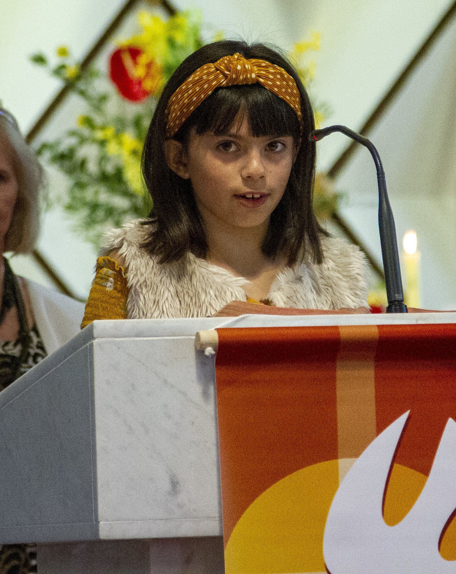 A little girl is sitting at a podium with a flame on it
