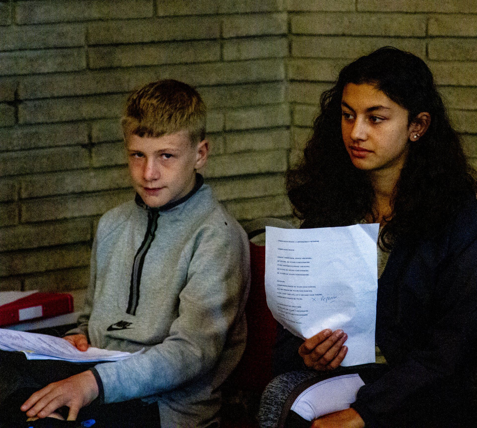 A boy and a girl are sitting in front of a brick wall