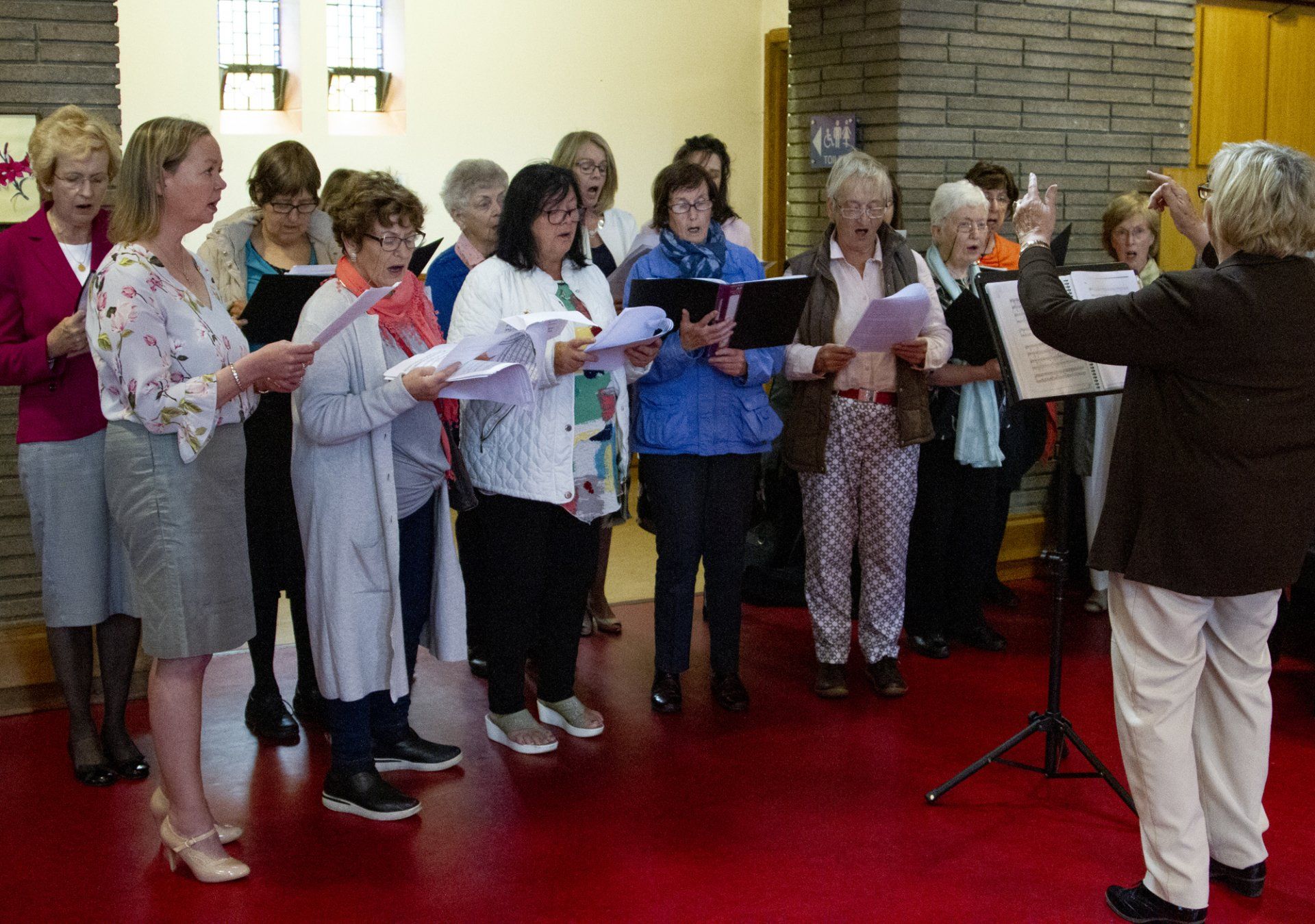 A woman is standing in front of a group of women singing in a choir.