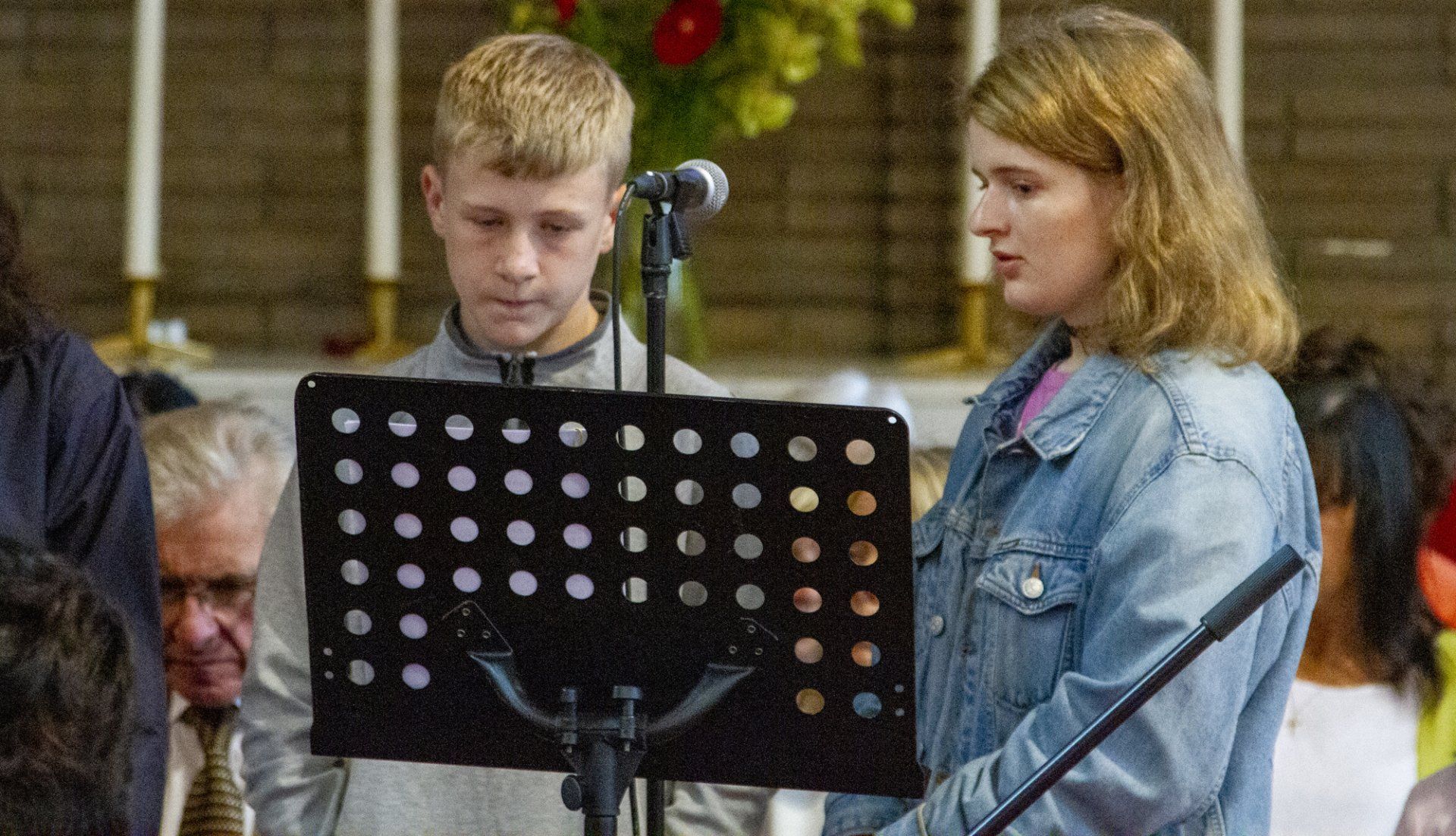 A boy and a girl are singing into microphones in a church.