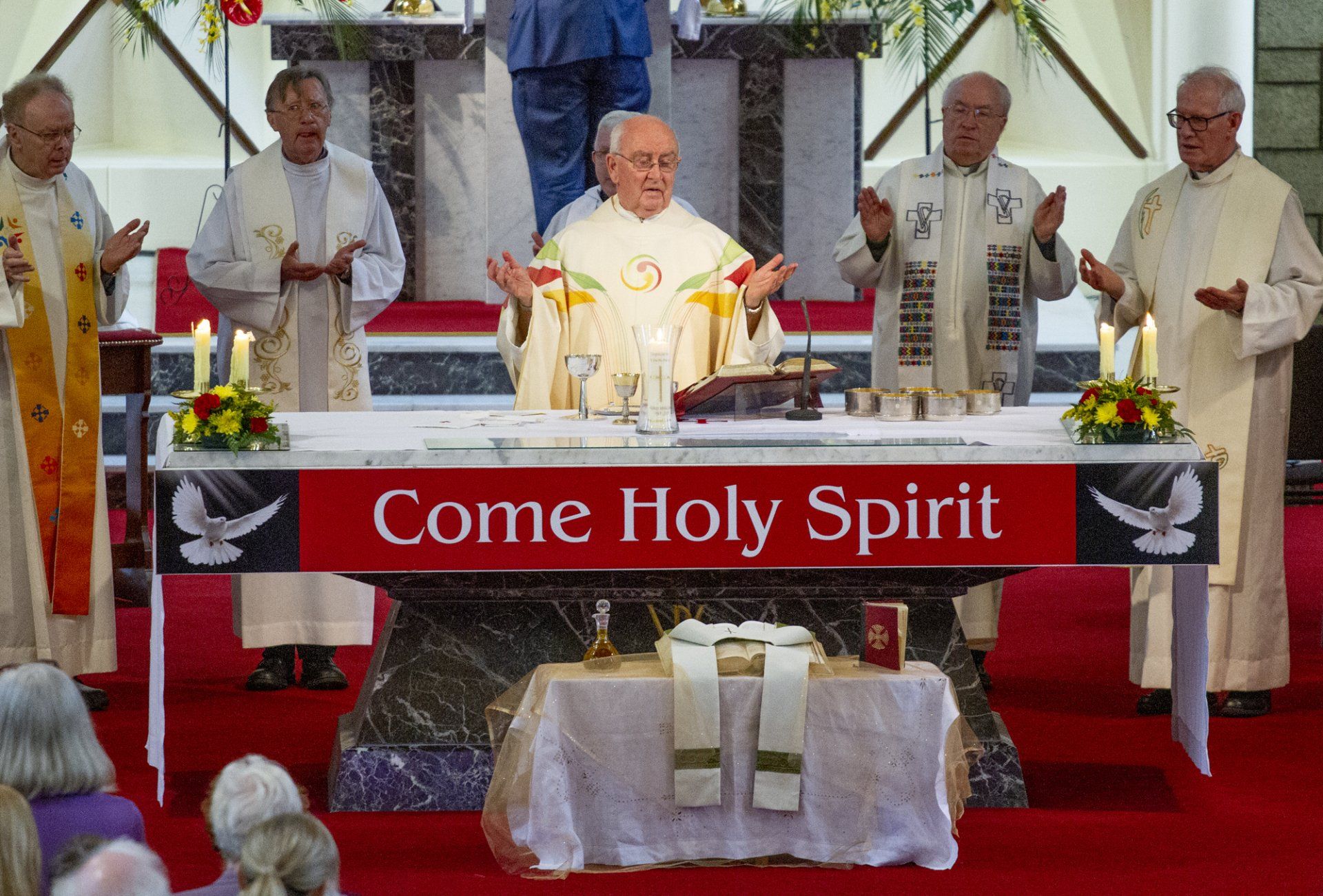 A group of priests are standing around an altar with a sign that says come holy spirit