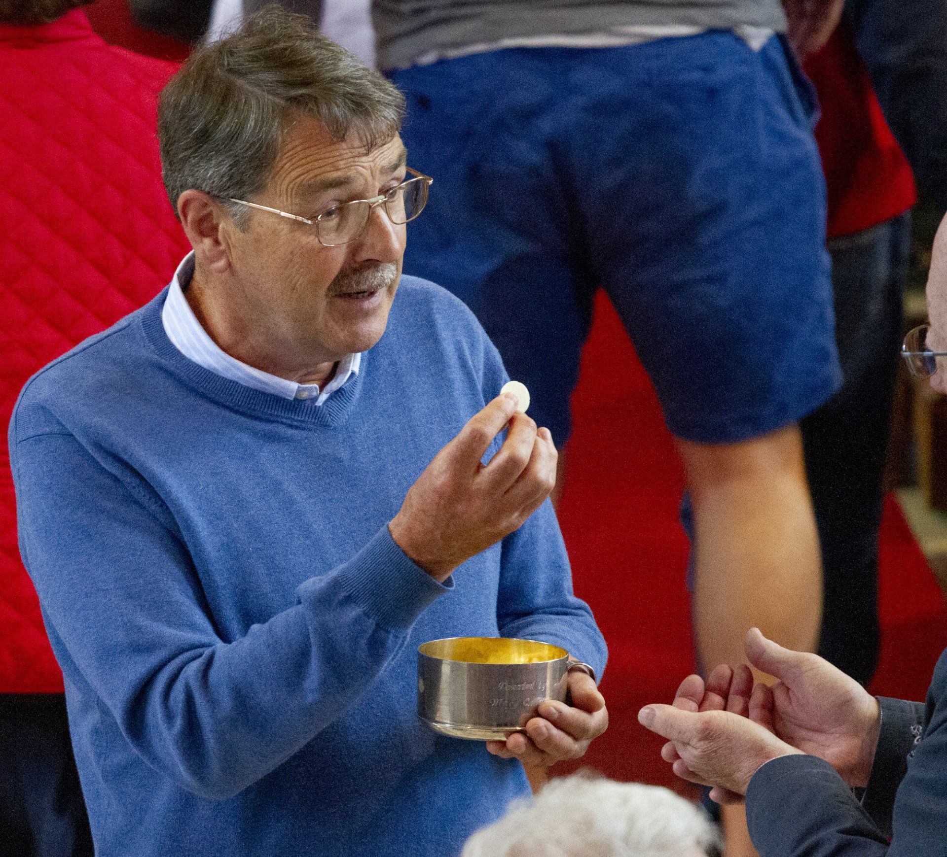 A man in a blue sweater is holding a cup of communion