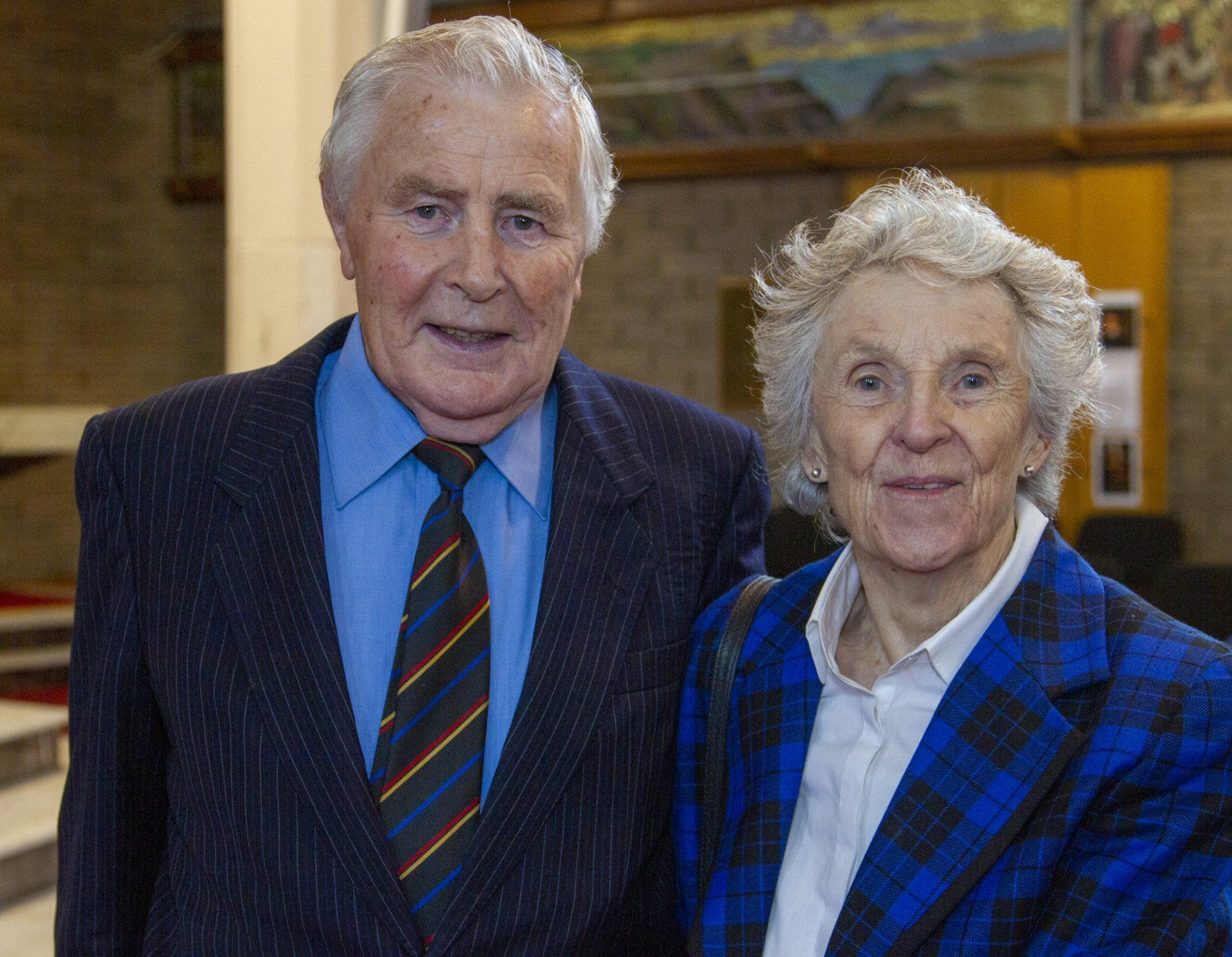 A man in a suit and tie is standing next to a woman in a blue jacket.