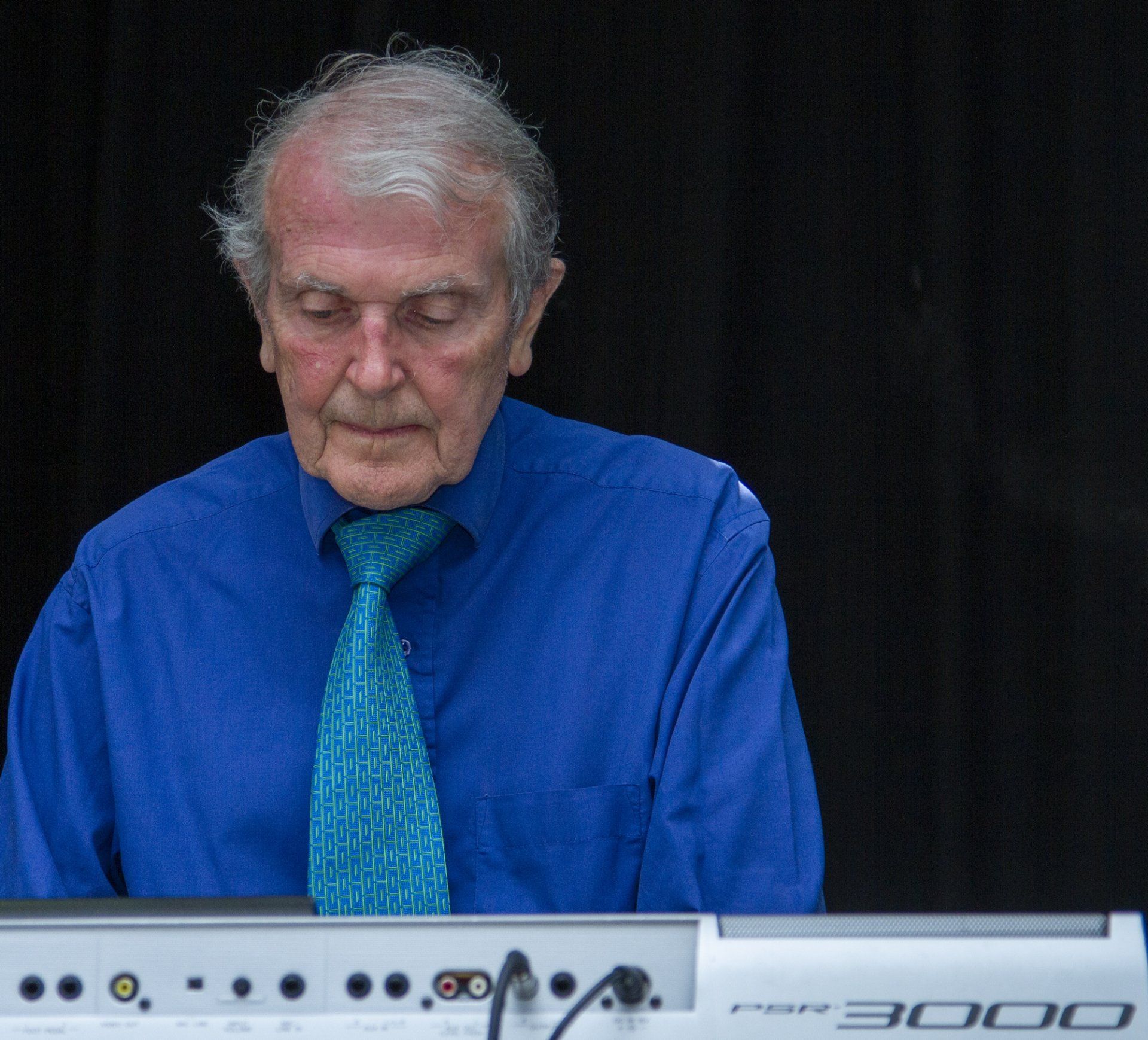 A man in a blue shirt and tie is playing a keyboard with the number 3000 on it