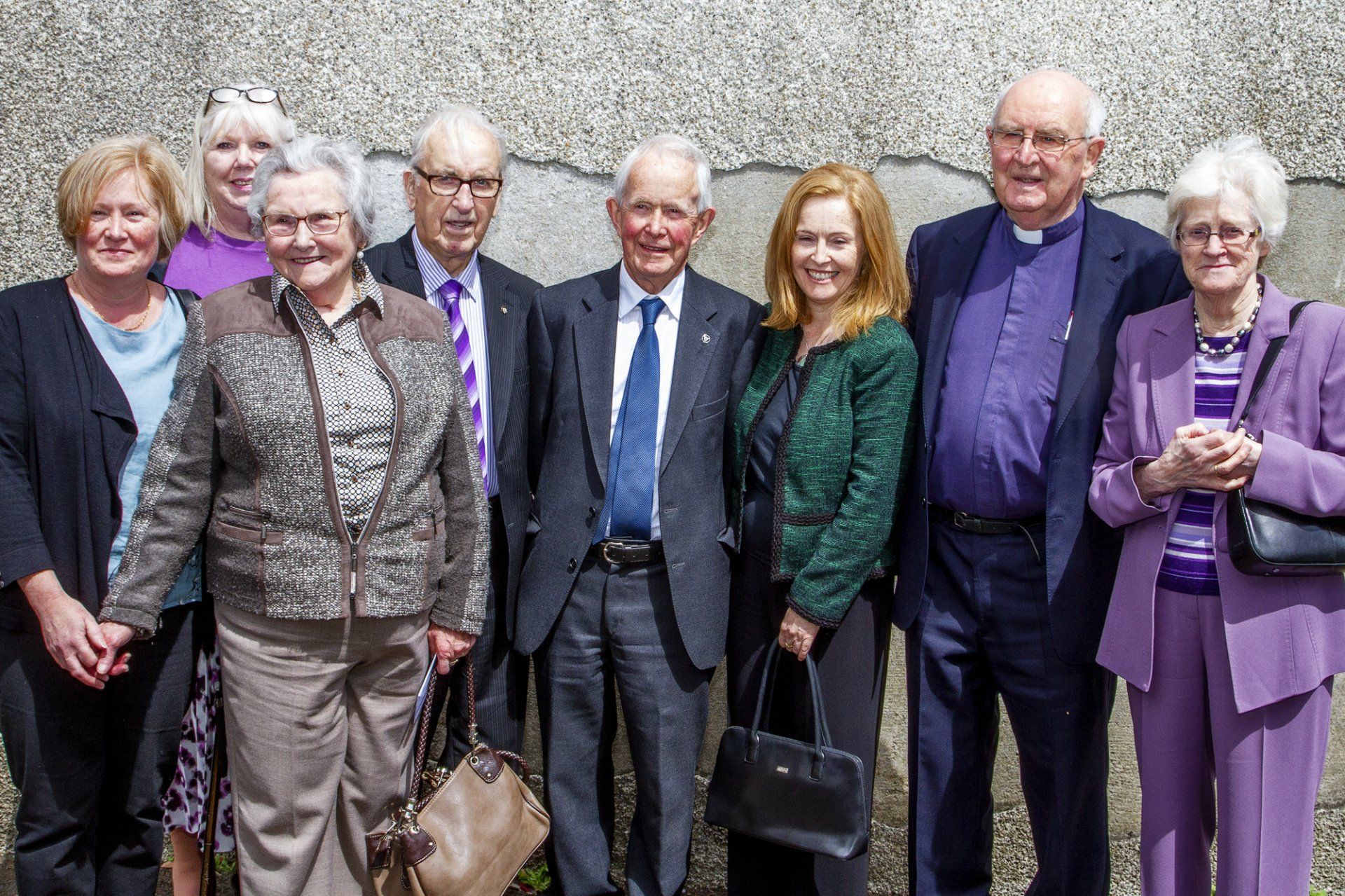 A group of people standing next to each other in front of a wall.