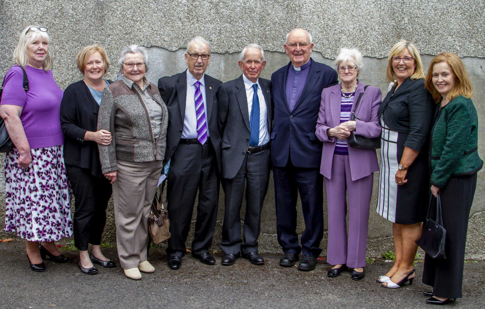 A group of people standing next to each other in front of a wall.