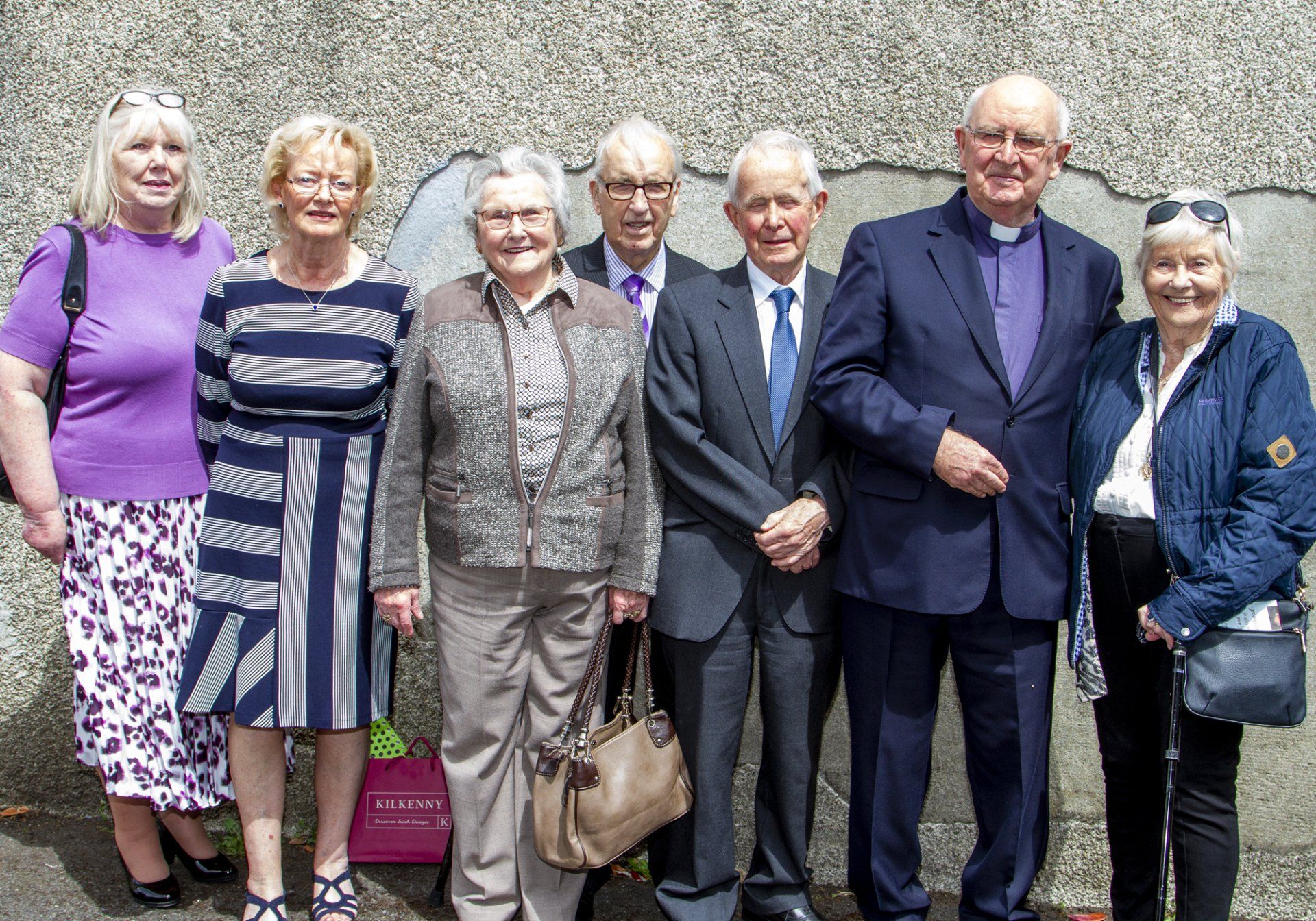 A group of people standing next to each other in front of a wall.