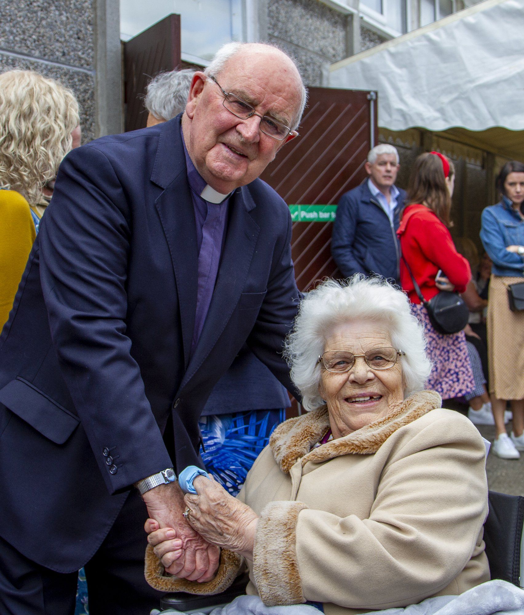 A man in a suit is shaking hands with an elderly woman in a wheelchair