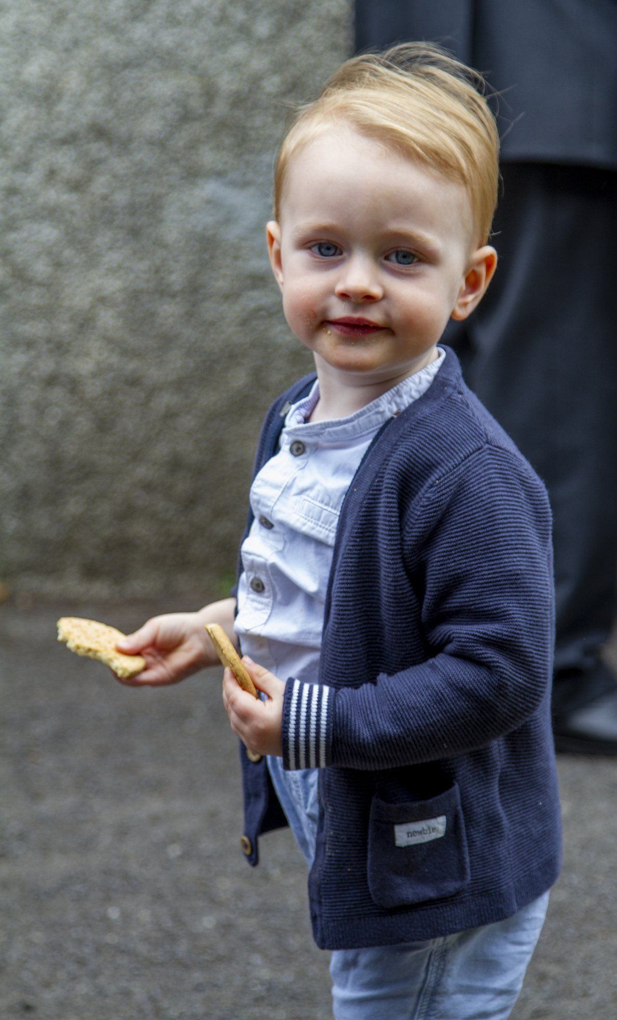 A little boy in a blue cardigan is holding a cookie in his hand.